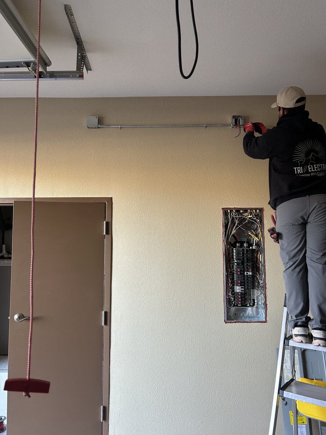 Electrician on a ladder running conduit above a residential panel during a service upgrade